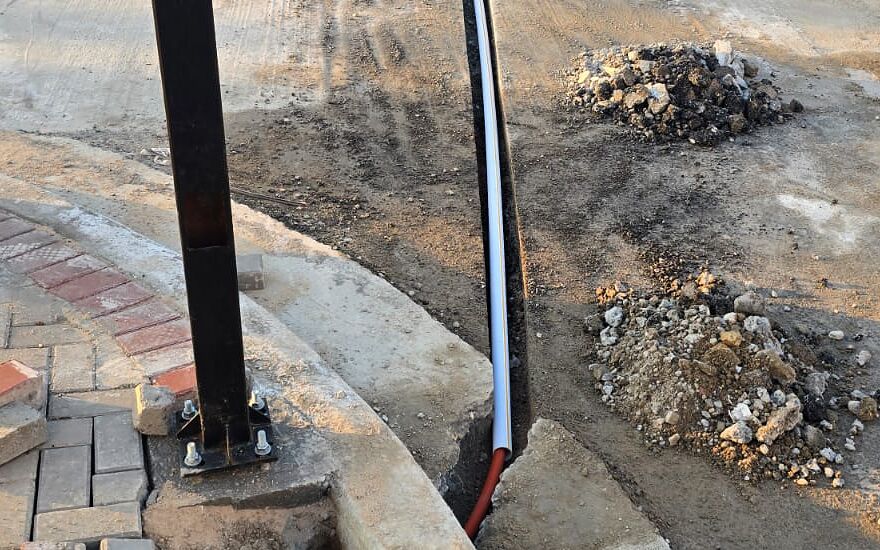 Bolted steel camera pole and underground cable conduit routed through a curb trench during installation at the Asad Babel site