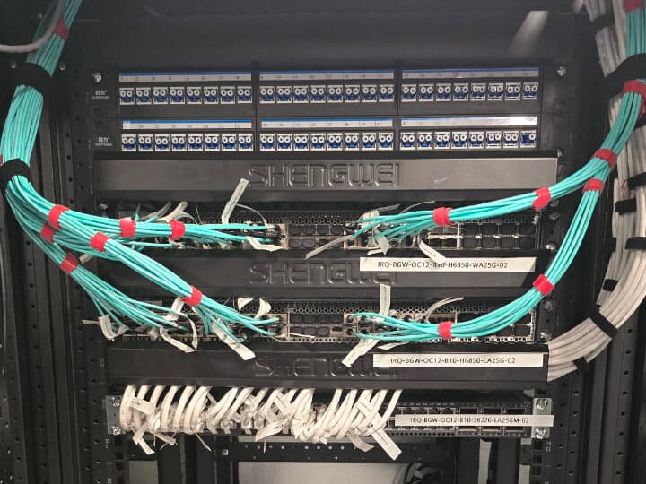 Rack-mounted fibre patch panels and network switches, with aqua fibre patch leads bundled, banded and labelled across the front of the cabinet