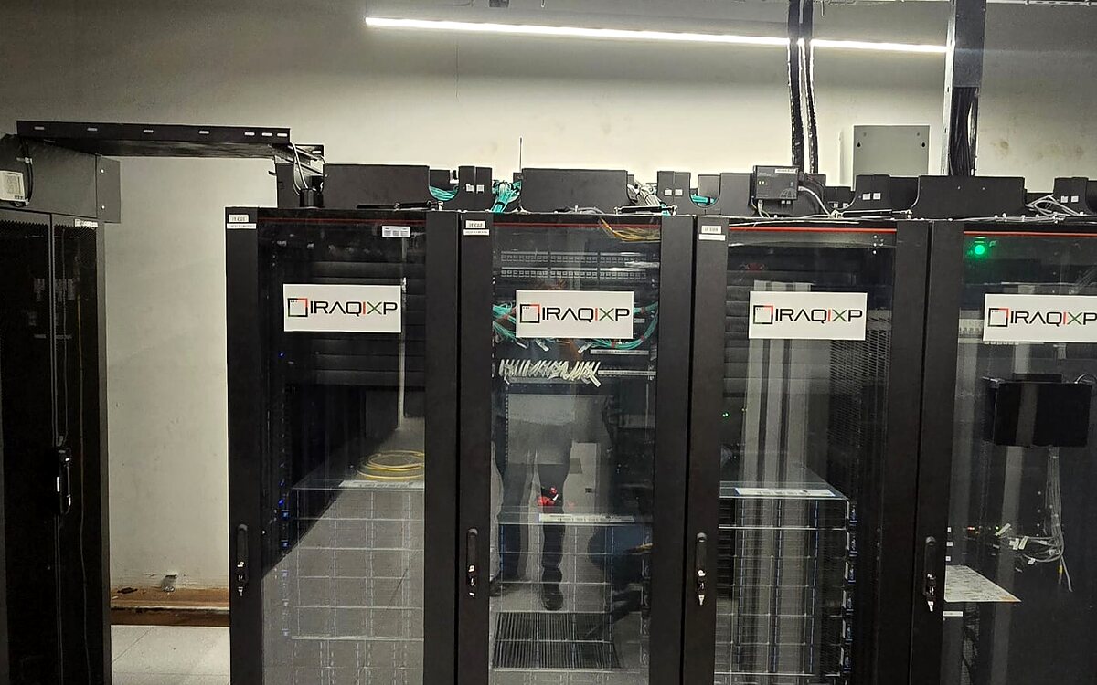 Row of IraqIXP-branded server racks with glass doors in a data center aisle, cable trays and structured cabling overhead